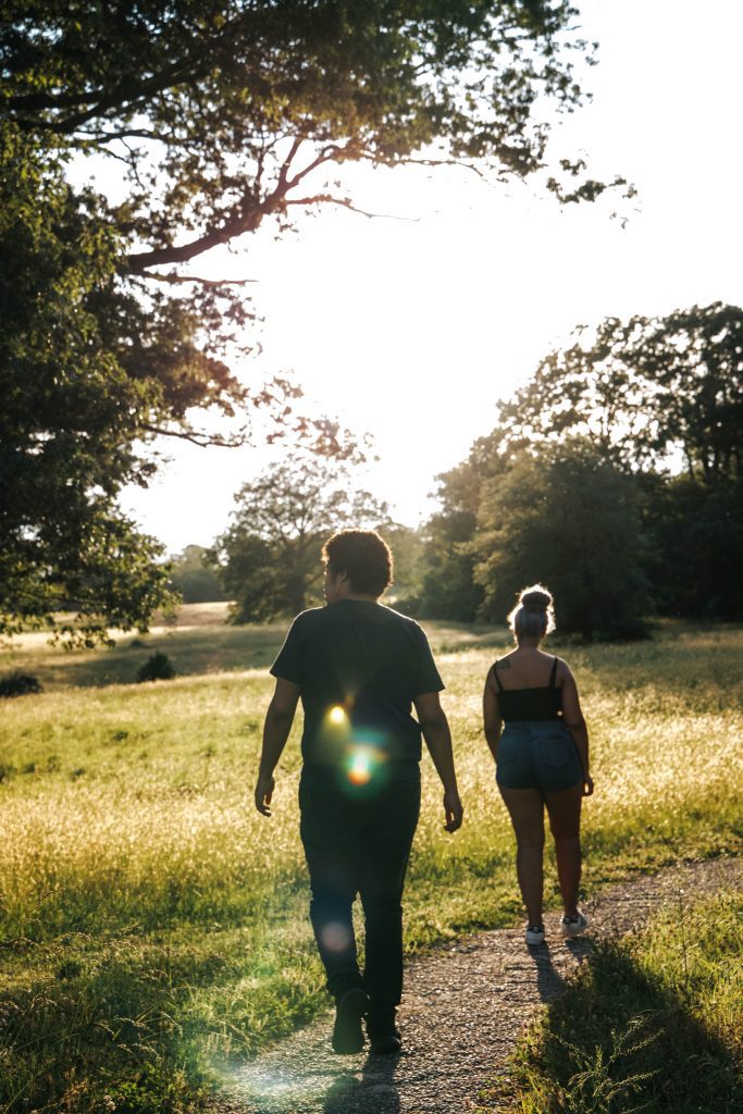 Un homme et une femme marchent au bord de la route, devant un champ et quelques arbres